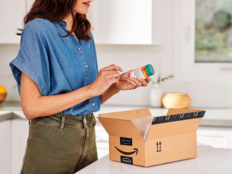 A woman stands over a box from Amazon RxPass through Amazon Pharmacy with a prescription bottle in her hand.