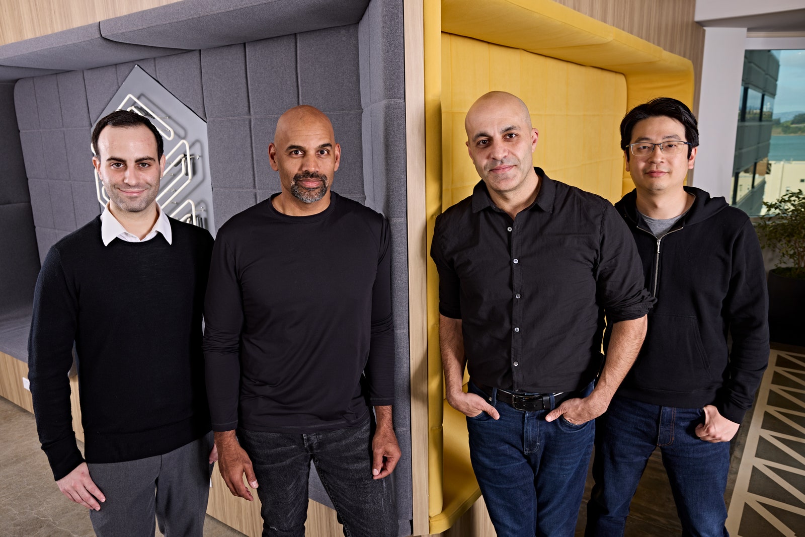 Four people standing at the corner of a grey and yellow wall in an office space